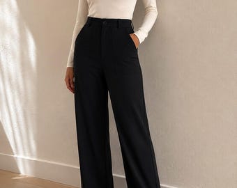 May include: A long-sleeved cream-colored crew neck top paired with high-waisted black wide-leg trousers. The trousers feature a button closure, a front zipper, and two large patch pockets on the front. The outfit is completed with black pointed-toe shoes.