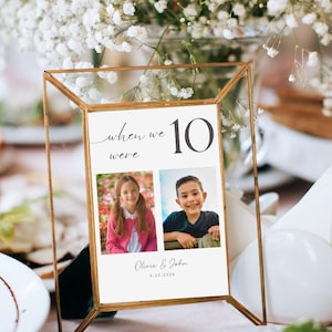 May include: A gold-framed table number card with the text "when we were 10" and two photos of children. The names "Olivia & John" and the date "6.25.2026" are also printed on the card. The card is on a table with flowers.