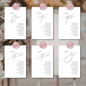 Puede incluir: Seis tarjetas de mesa blancas con caligrafía elegante, cada una coronada con un sello de cera rosa con un diseño de lazo. Las tarjetas están etiquetadas con números y nombres de invitados, perfectas para bodas o eventos.