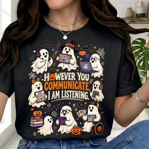 May include: A black t-shirt featuring a graphic of multiple white ghosts using various communication devices, including tablets and laptops. The text reads, "HOWEVER YOU COMMUNICATE, I AM LISTENING." The design includes pumpkins, bats, and spiderwebs.