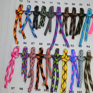 May include: A color chart featuring numbered samples of braided cord in various patterns and colors, including neon pink, camouflage, black and white, and multi-colored geometric designs, each tied in a simple knot and attached to a white card.