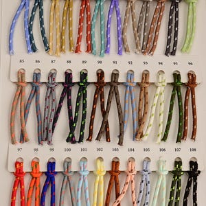 May include: A color chart featuring thirty-six individual samples of braided cord, each knotted and numbered from 73 to 108. The cords display a variety of solid colors and patterns, including blue, green, yellow, red, brown, black, and white.