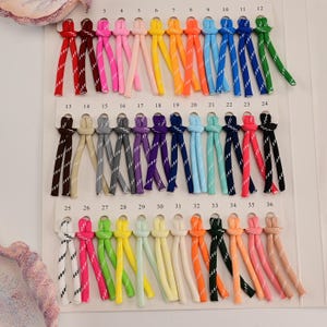 May include: A collection of thirty-six pairs of colorful nylon cords arranged in three rows on a white display card. Each cord features a reflective white diagonal stripe pattern and is knotted at the top, numbered from 1 to 36.