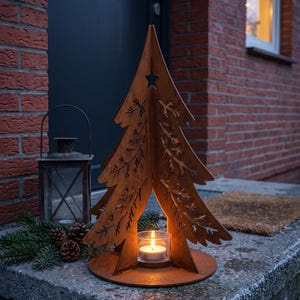Può includere: Una decorazione natalizia a forma di albero in metallo color ruggine con un motivo a rami intagliati e una stella sulla punta. L'albero poggia su una base circolare e presenta un centro aperto che ospita un portacandele in vetro con candela.
