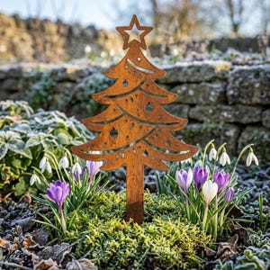 Può includere: Un picchetto da giardino in metallo color ruggine a forma di albero di Natale, con una stella ritagliata sulla punta e ornamenti circolari tra i rami. L'albero è posizionato in un'aiuola con crochi viola e bucaneve bianchi.