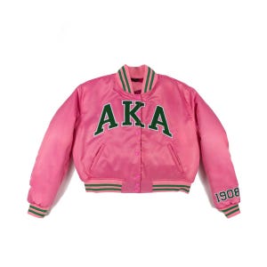 Op de afbeelding: Een roze satijnen bomberjack met de letters "AKA" in groen over de borst. De jas heeft groen-witte gestreepte randen op de kraag, manchetten en zoom, en het nummer "1908" staat op de linkermouw.