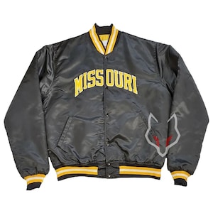 Könnte beinhalten: Schwarze Satin-Bomberjacke mit gelb-weißem Streifenbesatz. Die Jacke trägt den Schriftzug "MISSOURI" in gelben Blockbuchstaben auf der Brust und eine stilisierte Wolfsgrafik auf dem Ärmel.