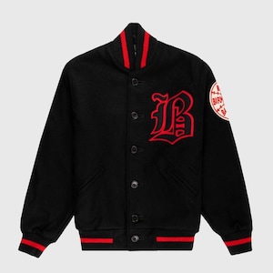 Könnte beinhalten: Schwarze Collegejacke mit roten Akzenten. Auf der Brust befindet sich ein großes rotes "B" und ein Aufnäher auf dem Ärmel. Kragen, Bündchen und Saum sind rot gestreift. Mit Knopfverschluss.