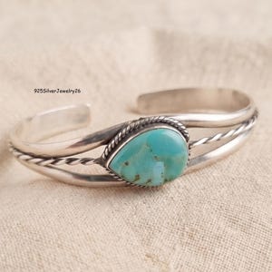May include: A silver cuff bracelet featuring a central teardrop-shaped turquoise stone with brown matrix, surrounded by a twisted wire border. The band consists of two smooth silver wires and one twisted wire. Text 925SilverJewelry26 is visible.