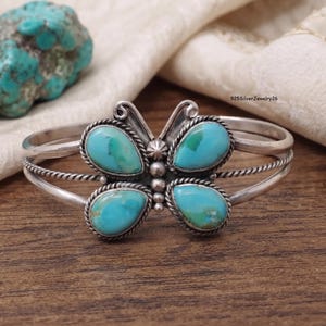 May include: A sterling silver cuff bracelet featuring a butterfly design with four teardrop-shaped turquoise stones. The bracelet has a twisted wire band and a central vertical row of small silver beads. The text 925SilverJewelry26 is visible.