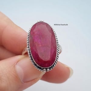 Könnte beinhalten: Ein Ring aus Sterlingsilber mit einem großen, ovalen, facettierten, tiefrosa Edelstein, der in eine gedrehte, seilartige Metallfassung eingefasst ist. Die Ringschiene ist aus schlichtem Silber. Der Text 925SilverJewelry26 ist oben rechts sichtbar.