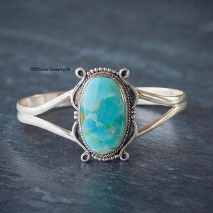 May include: A sterling silver cuff bracelet featuring a large, oval-shaped turquoise stone with blue and green marbling. The setting includes a twisted rope border and decorative scrollwork accents. The text 925SilverJewelry26 is visible.