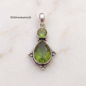 May include: A sterling silver pendant featuring a faceted pear-shaped peridot stone at the base and a smaller round faceted peridot stone above it, set in a decorative metal frame with beaded accents and a bail, with the text 925SilverJewelry26.