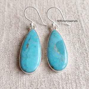May include: A pair of teardrop-shaped turquoise earrings set in silver with curved ear wires. Each stone features natural blue and green veining. The text 925SilverJewelry26 is visible in the upper right corner of the image.