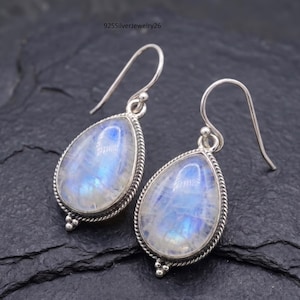 May include: A pair of teardrop-shaped earrings with a silver-colored metal frame. The earrings feature a pearlescent, blue-white stone with a textured appearance. The frame has a twisted rope design around the stone and a simple hook.