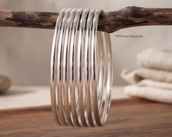 May include: A set of seven thin, polished silver bangles arranged in a row. The bracelets have a smooth, reflective metallic surface and a rounded profile. The text 925SilverJewelry26 is visible in the upper right area of the image.