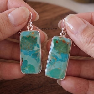 Puede incluir: Un par de pendientes rectangulares colgantes con piedras de turquesa pulidas con vetas naturales en azul y verde, engastadas en marcos de plata con ganchos de plata. El texto 925SilverJewelry26 es visible en el centro de la imagen.