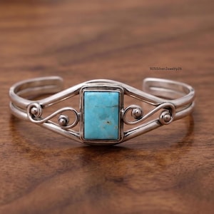 May include: A silver cuff bracelet featuring a rectangular turquoise stone set in the centre. The metal band displays decorative swirling wire details on both sides of the stone. The text 925SilverJewelry26 is visible in the upper right corner.
