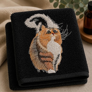 May include: A black hand towel featuring an embroidered design of a fluffy orange and white cat with a large, bushy tail. The cat is depicted in a seated position with its head turned upward, showcasing detailed stitching in shades of orange, white, and black.