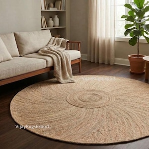 Op de afbeelding: Een grote, ronde jute vloerkleed met een concentrisch spiraalontwerp domineert de voorgrond. Het vloerkleed heeft een natuurlijke bruine kleur, die past bij de houten vloer en de beige bank op de achtergrond. Gezellige woonkamer.