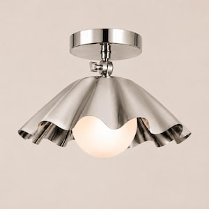 May include: A polished silver-tone metal ceiling light fitting featuring a wide, scalloped, bell-shaped shade. A single, spherical, frosted white glass bulb is centred beneath the metallic shade, which is attached to a circular mounting plate.