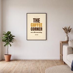 Op de afbeelding: Een rechthoekige wandkunstprint in een zwarte lijst met een crèmekleurige achtergrond, voorzien van de tekst THE COFFEE CORNER in dikke bruine en gouden letters, met de ondertitel est. this morning. en drie kleine koffieboonpictogrammen.