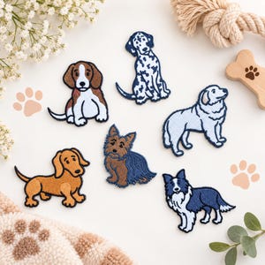 May include: A collection of six embroidered dog patches featuring various breeds including a brown and white beagle, a spotted dalmatian, a fluffy white dog, a long-bodied brown dachshund, a small brown terrier, and a black and white border collie.