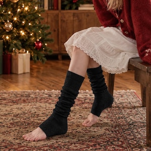 May include: A pair of dark charcoal gray knit leg warmers featuring a ribbed texture that extends from the mid-calf down to the ankle, leaving the heel and toes exposed. The leg warmers are crafted from a soft, textured yarn material.
