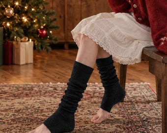 May include: A pair of dark charcoal gray knit leg warmers featuring a ribbed texture that extends from the mid-calf down to the ankle, leaving the heel and toes exposed. The leg warmers are crafted from a soft, textured yarn material.