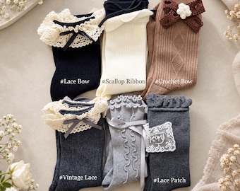May include: Six pairs of ribbed socks in black, cream, brown, dark gray, and light gray. Features include a black lace bow, a cream scallop ribbon, a brown crochet bow, vintage lace trim, a ribbon wave detail, and a white lace patch.