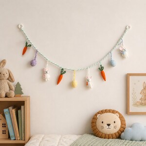 Puede incluir: Una guirnalda decorativa que presenta una cuerda trenzada de color azul claro y blanco con adornos de ganchillo colgantes, incluyendo zanahorias naranjas, huevos de tonos pastel y peque&ntilde;os conejos blancos, suspendida horizontalmente.