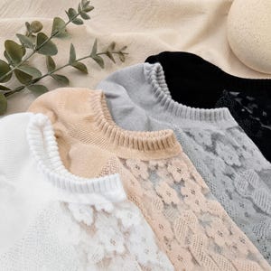 Puede incluir: Primer plano de cuatro pares de calcetines invisibles en blanco, beige, gris y negro. El par blanco tiene un delicado diseño de encaje, mientras que los pares beige y grises presentan patrones de encaje floral. El par negro tiene un diseño de encaje sutil. Los calcetines están hechos de un material suave y transpirable.