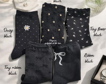 May include: Five pairs of black socks with various patterns, including daisies, tiny flowers, bows, and textured designs. The socks are labeled "Daisy black", "Prahlen black", "Tiny flower black", "Tiny ribbon black", and "Ribbon black". The text "Elegance, perfected at the toes" is also visible.