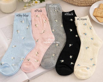 May include: Five pairs of floral patterned socks in sky blue, pink, gray, black, and cream. Each sock features a delicate floral design with small blue and white flowers. The socks are displayed on a white surface.