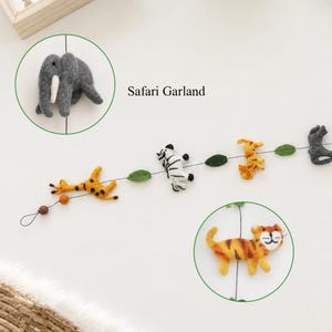 Puede incluir: Una guirnalda Safari con figuras de animales de fieltro, incluyendo una jirafa, una cebra, un tigre y un elefante, ensartadas en un cord&oacute;n fino con hojas de fieltro verde y peque&ntilde;as cuentas de madera.