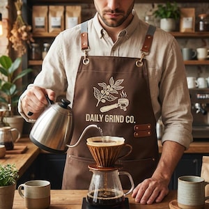 Puede incluir: Un barista vierte agua caliente de una tetera de acero inoxidable en una cafetera de goteo. El barista lleva un delantal marrón con el texto "DAILY GRIND CO." y un gráfico temático de café. El café se prepara en una jarra de vidrio.