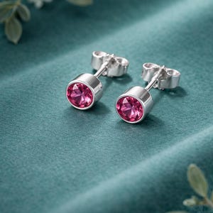 Op de afbeelding: Een paar zilveren oorstekers met helder roze edelstenen. De oorbellen zijn afgebeeld op een turquoise achtergrond. De tekst "PUREPAI JEWELRY", "925 STERLING SILBER" en "ONE EARRING ROSY" is zichtbaar.
