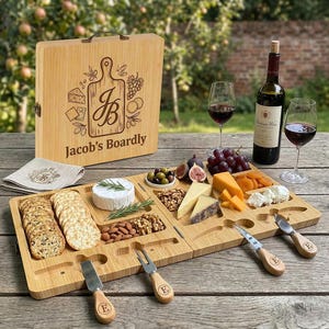May include: A bamboo cheese board set with a handle, engraved with "Jacob's Boardly" and a cutting board design. The set includes cheeses, crackers, nuts, olives, figs, and grapes, alongside wine glasses and a bottle of wine.
