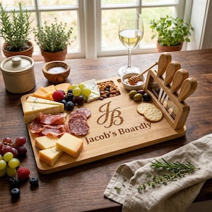 May include: A wooden serving board laden with cheese, cured meats, grapes, and nuts. The board features cheese knives and the engraved text "Jacob's Boardly". A wine glass and potted herbs are visible in the background, near a window.