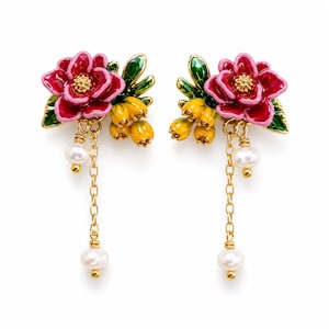 Puede incluir: Un par de pendientes dorados con flores rosas esmaltadas de centro amarillo, hojas verdes y racimos de pequeños capullos amarillos. Cada pendiente incluye una cadena dorada con dos perlas blancas de diferentes tamaños.