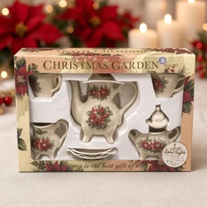 May include: A Christmas Garden tea set in a cardboard box featuring a cream-colored teapot, creamer, sugar bowl with lid, and two cups, all decorated with red poinsettia floral patterns. The box includes the text Christmas Garden and TLA Set.