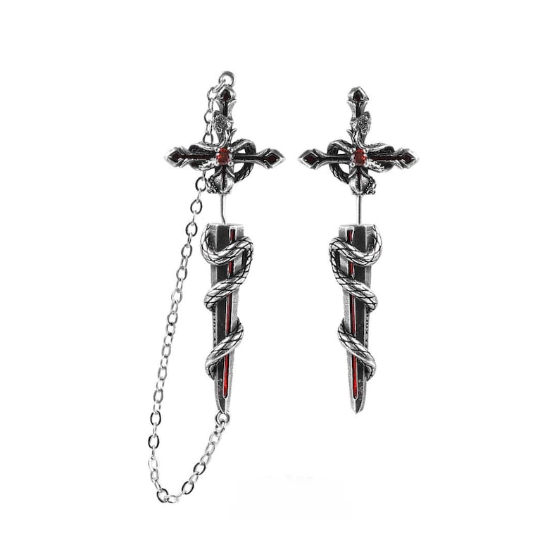May include: A pair of silver-toned earrings featuring a dagger and cross design. Each earring has a snake coiled around the blade, which is accented with a red centre. One earring includes a delicate silver chain connecting the cross to the dagger.