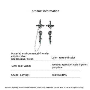 May include: A pair of silver-toned earrings featuring a cross design with a central green zircon, connected to a dagger-shaped pendant wrapped in a snake motif. One earring includes a delicate chain. Dimensions are 18.8 by 50 mm, weighing 5 grams.