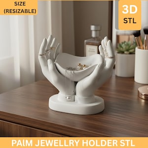 May include: A white ceramic jewelry holder in the shape of hands, with a small bowl in the center. The hands are holding the bowl, which contains jewelry. Rings are on the fingers. The base is round. The text "PALM JEWELLRY HOLDER STL" is at the bottom.