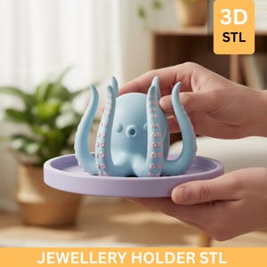 Könnte beinhalten: Ein hellblaues, tintenfischförmiges Schmuckhalter mit rosa Akzenten, auf einem lila Tablett. Der Text "JEWELLERY HOLDER STL" befindet sich unten, mit "3D STL" in einer gelben Box. Der Halter wird von einer Person gehalten.