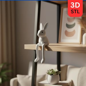 May include: A white bunny figurine with long legs, sitting on a wooden shelf. The bunny is a decorative item, with a minimalist design. The shelf is part of a black metal shelving unit. A framed artwork and a potted plant are also visible.