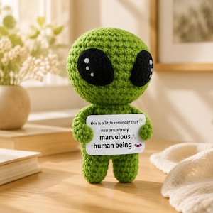 May include: A green crocheted alien figure with large black eyes and a small white card. The card reads "this is a little reminder that you are a truly marvelous human being."