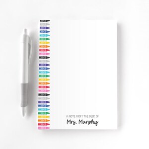 May include: A white notepad with a colorful crayon border and a matching pen. The notepad has the text "A note from the desk of Mrs. Murphy" printed on it. The pen is gray and white.