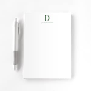 May include: A white notepad with a green letter "D" and the text "jordan donaldson" printed on the top. A white pen is next to the notepad.