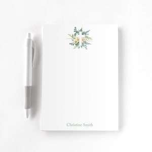 May include: White notepad with a green floral design and a white cross in the centre. The notepad has the name "Christine Smith" printed at the bottom.